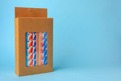 Box with many paper drinking straws on light blue background. Space for text