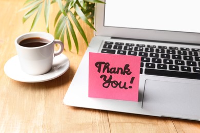 Photo of Pink paper note with phrase Thank You, laptop and coffee on wooden table