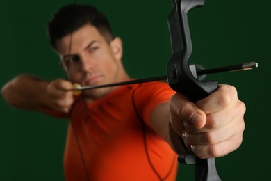 Photo of Man with bow and arrow practicing archery against green background, focus on hand