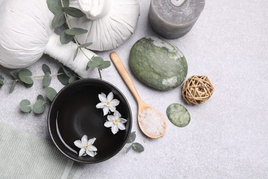 Flat lay composition with herbal massage bags, spa products and flowers on light grey table