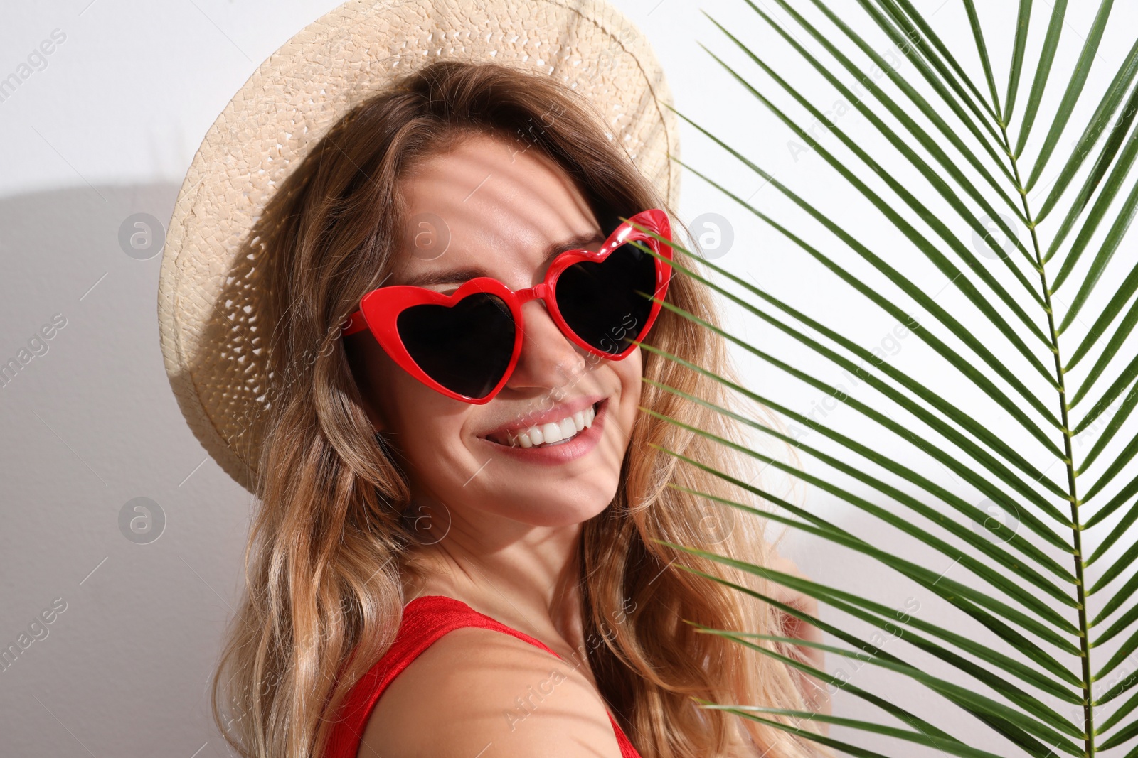 Photo of Young beautiful woman wearing heart shaped glasses and tropical palm leaf on white background