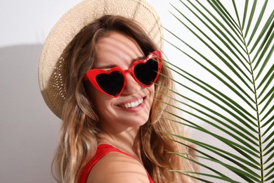 Photo of Young beautiful woman wearing heart shaped glasses and tropical palm leaf on white background