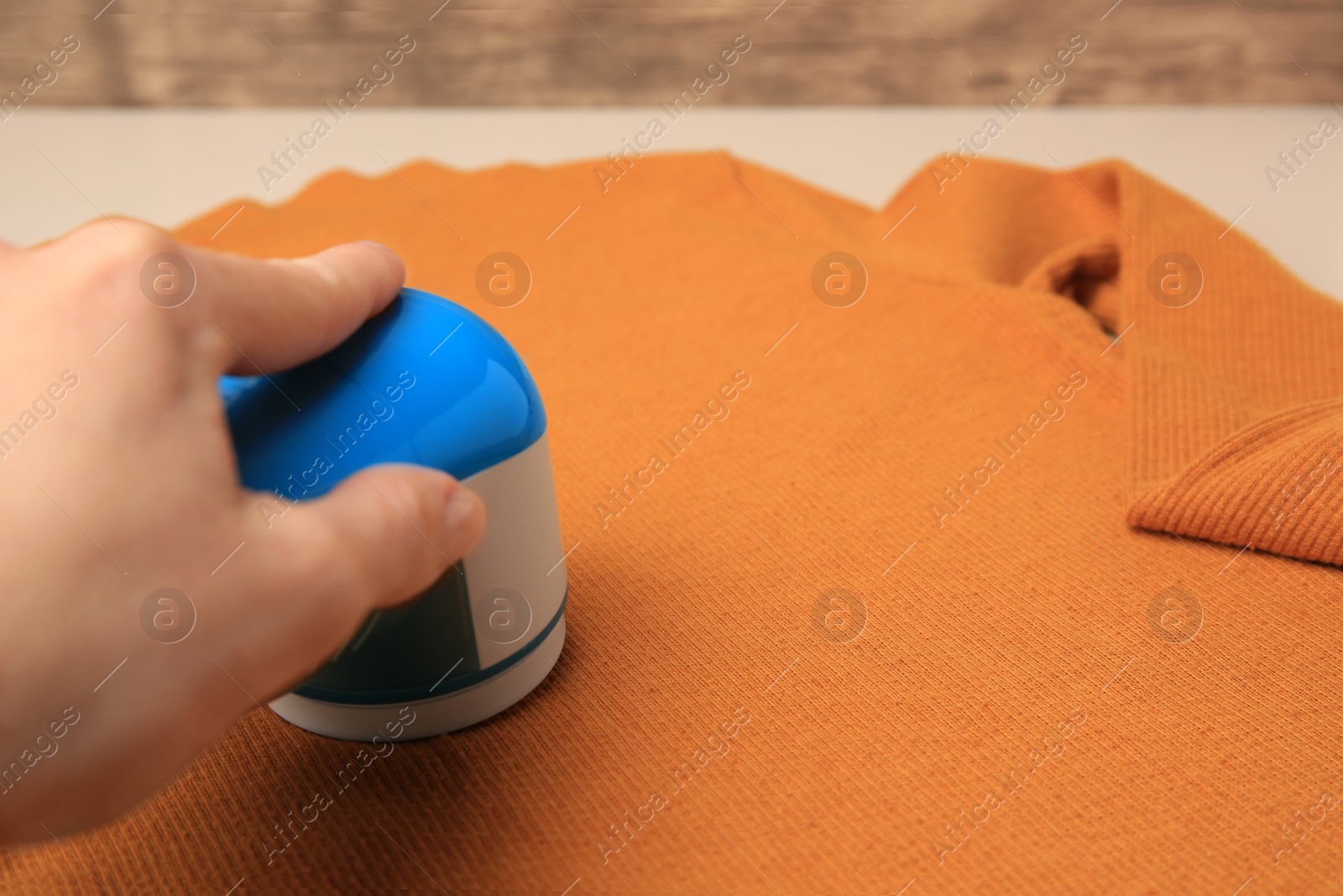 Photo of Woman using fabric shaver with orange sweater on beige background, closeup. Space for text