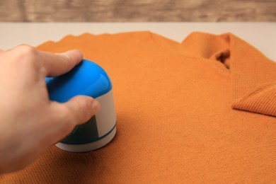 Woman using fabric shaver with orange sweater on beige background, closeup. Space for text