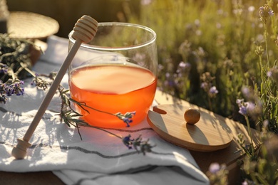 Photo of Jar of honey on wooden table in lavender field