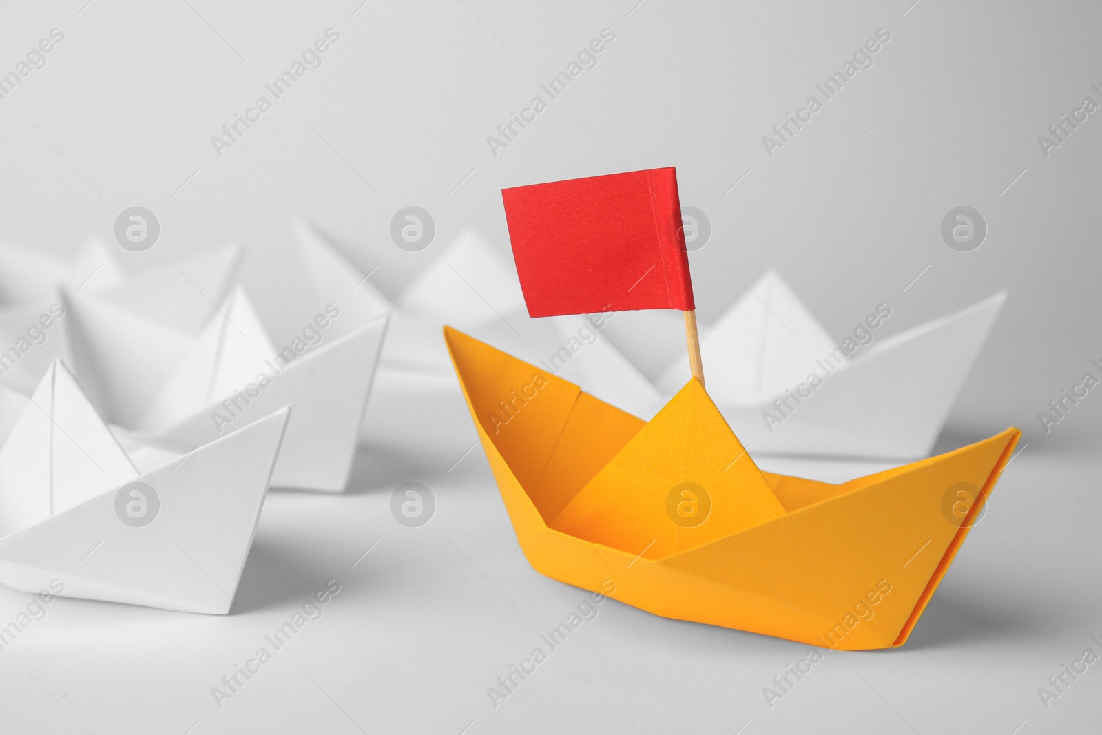 Photo of Group of paper boats following orange one on white background, closeup. Leadership concept