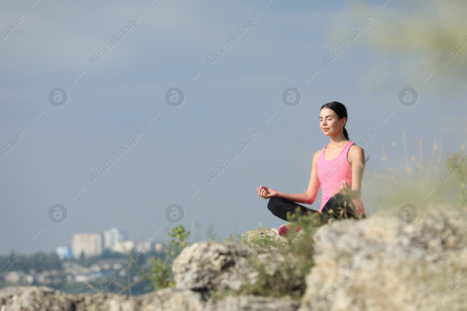 Photo of Young woman meditating on cliff. Space for text