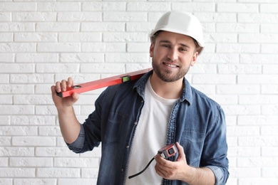 Photo of Young man with construction level and measuring tape near brick wall