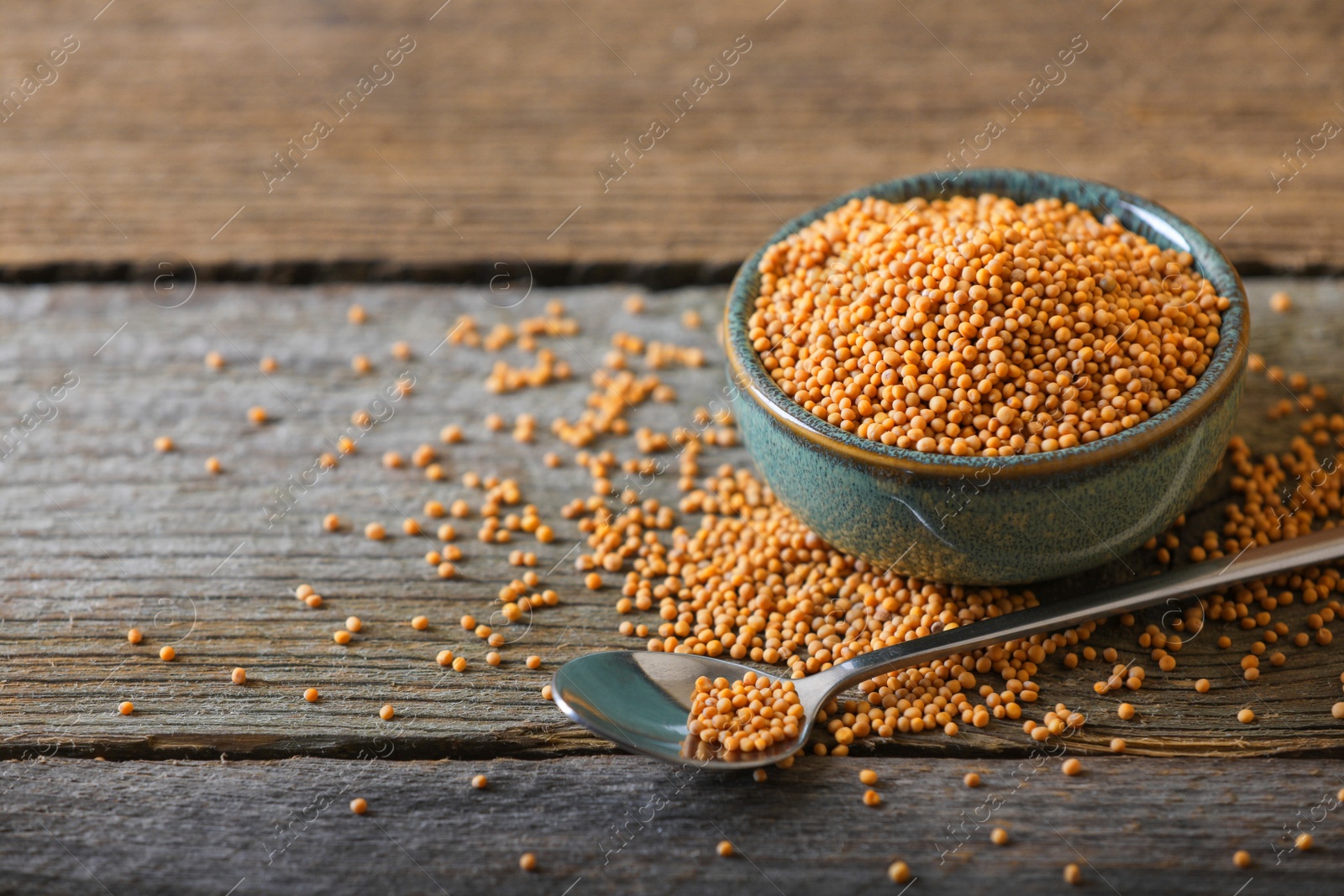 Photo of Bowl and spoon of mustard seeds on wooden table. Space for text