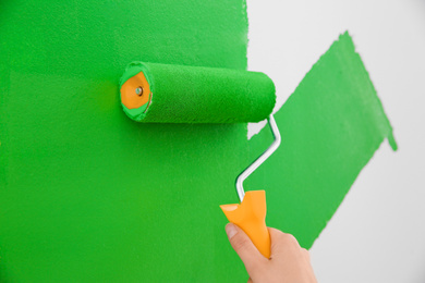 Photo of Woman painting white wall with green dye, closeup. Interior renovation