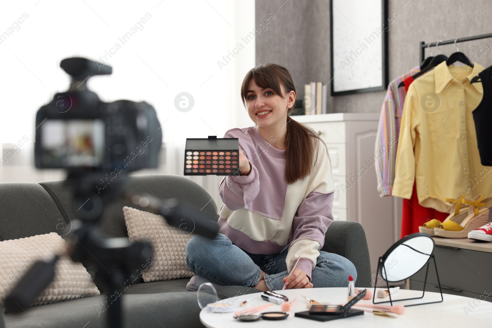 Photo of Smiling beauty blogger recording video while showing eyeshadow palette at home