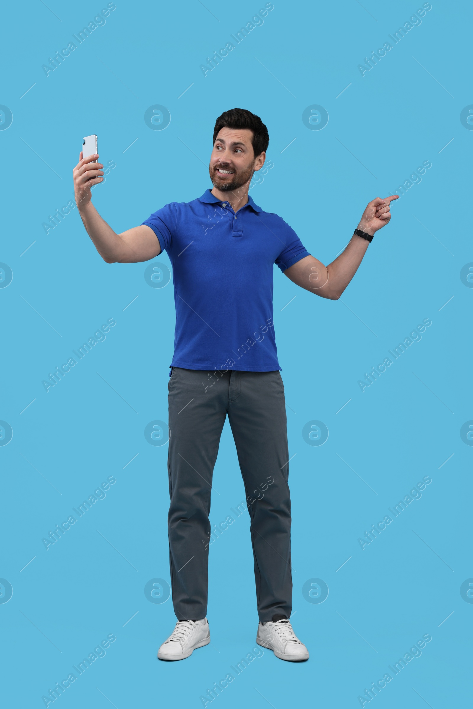 Photo of Smiling man taking selfie with smartphone on light blue background