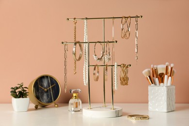 Photo of Holder with set of luxurious jewelry on dressing table near pale pink wall