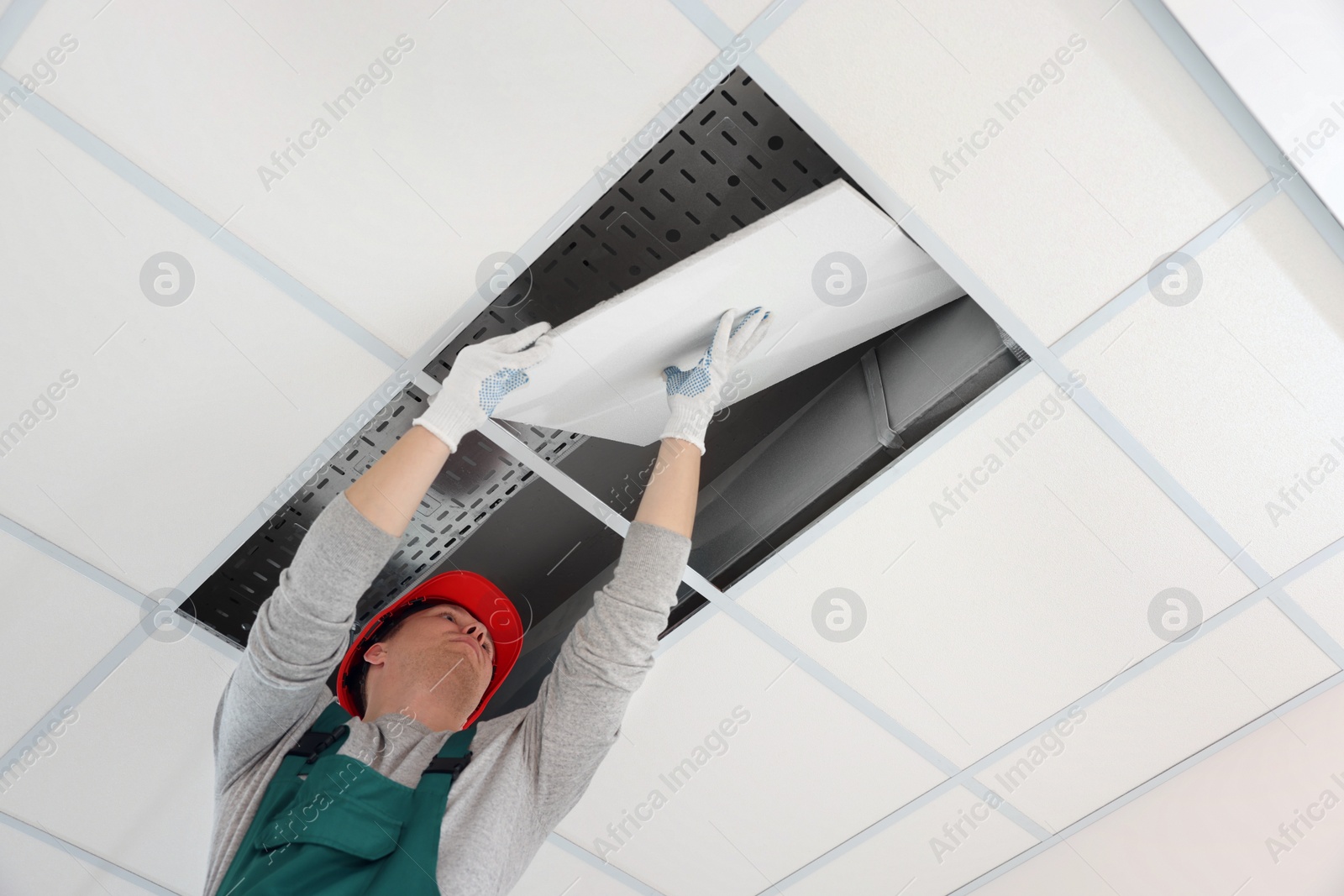 Photo of Suspended ceiling installation. Builder working with PVC tile, low angle view