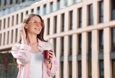 Photo of Young woman in sunglasses with plastic cup of fresh juice outdoors, space for text