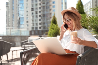 Photo of Beautiful woman with laptop and coffee talking on phone at outdoor cafe