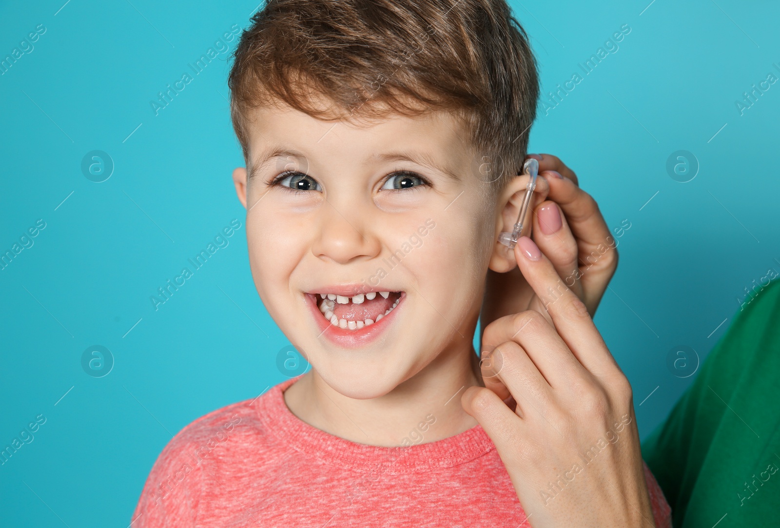 Photo of Young woman adjusting little son's hearing aid on color background, closeup