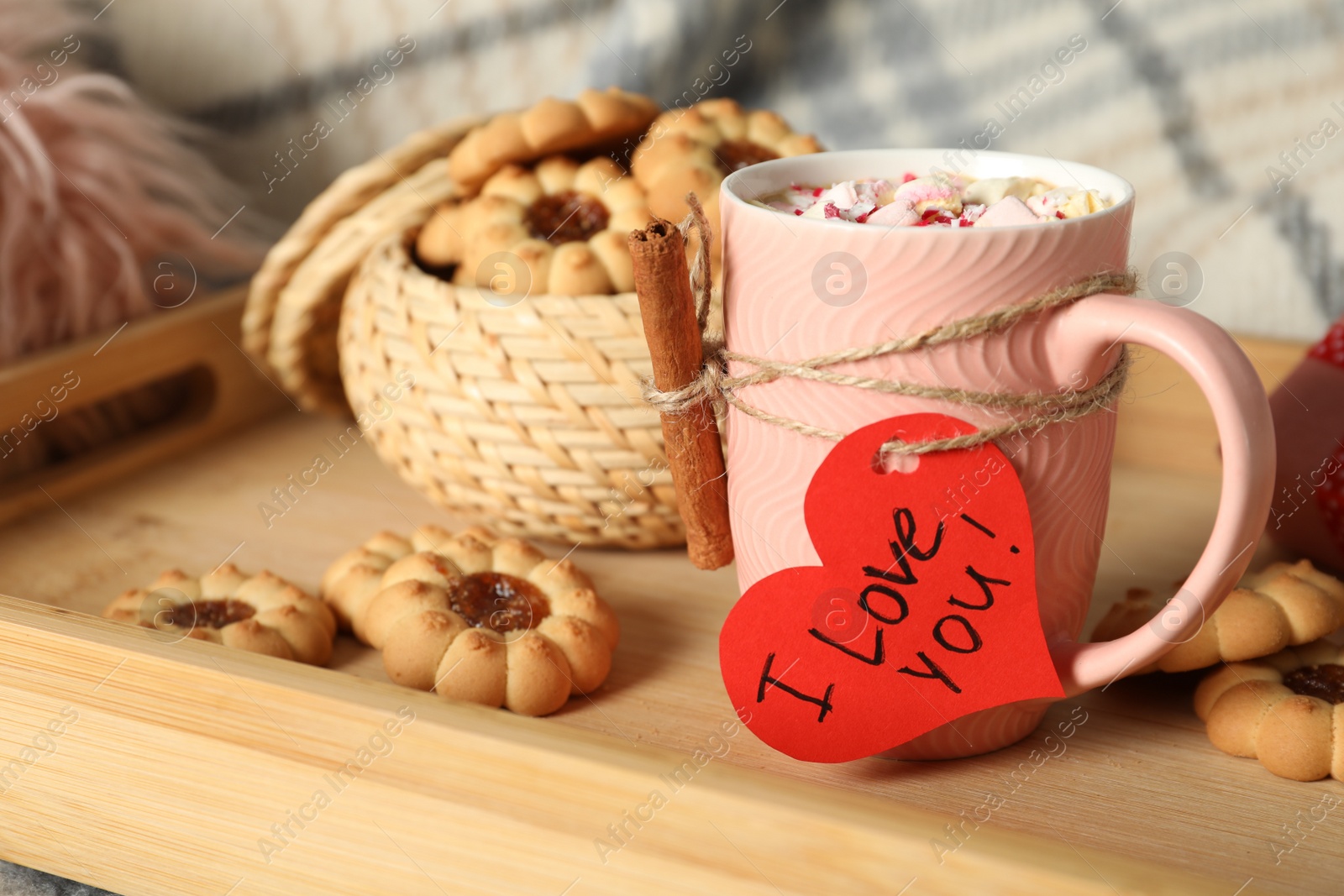 Photo of Heart shaped greeting card with phrase I Love You tied to pink cup near cookies on wooden tray