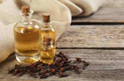 Essential oil and dried cloves on wooden table. Space for text