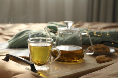 Photo of Wooden tray with freshly brewed tea and cookies on bed in room. Cozy home atmosphere