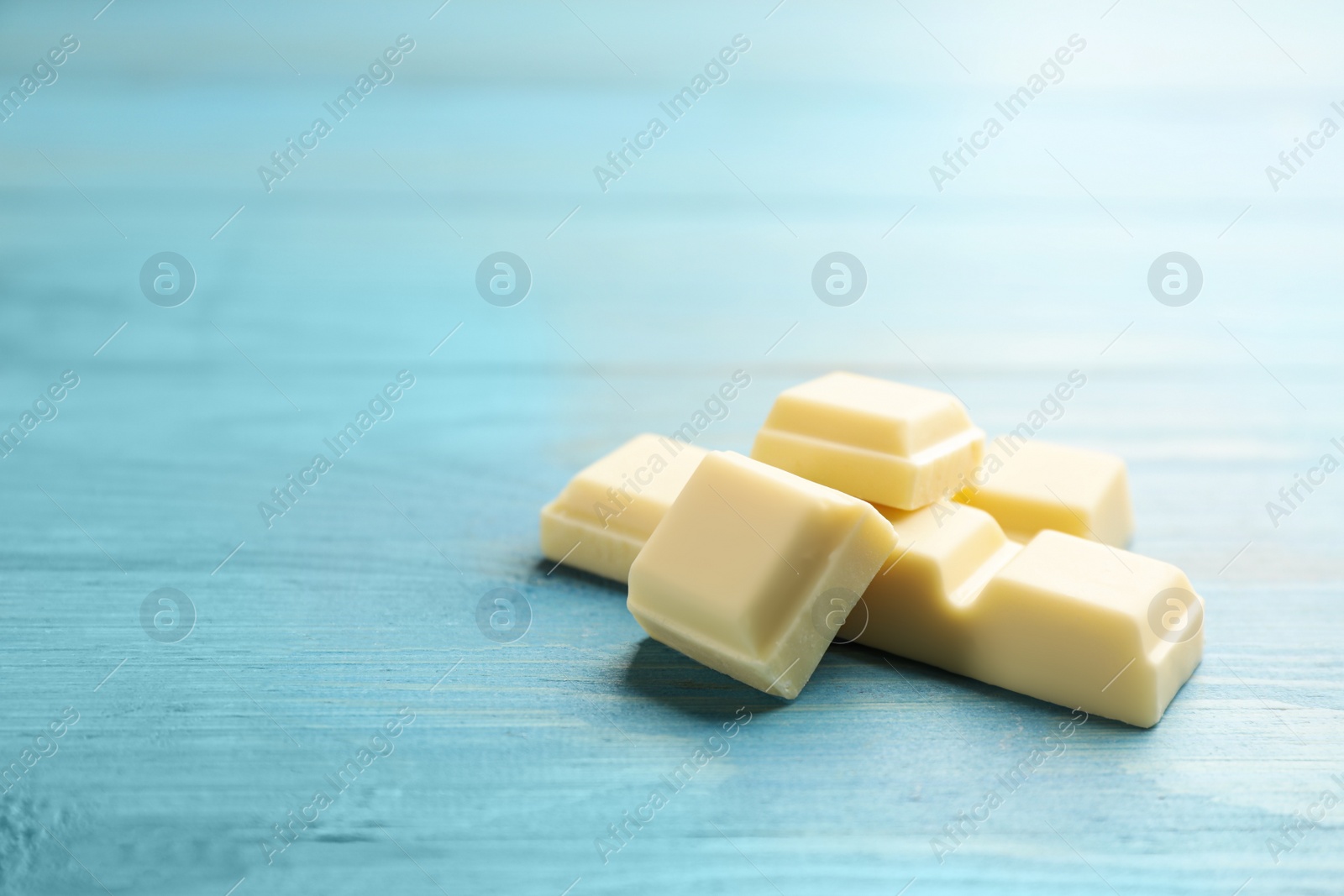 Photo of Pieces of tasty sweet chocolate on light blue wooden table, closeup. Space for text