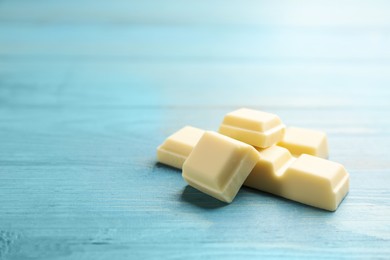 Pieces of tasty sweet chocolate on light blue wooden table, closeup. Space for text