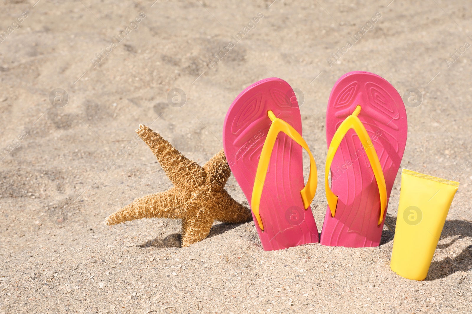 Photo of Stylish flip flops, sun protection cream and starfish on sand, space for text