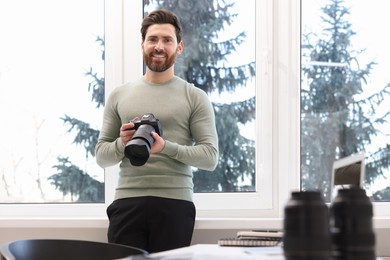 Professional photographer with digital camera near window indoors