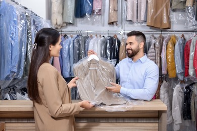 Photo of Dry-cleaning service. Happy worker giving jacket to client indoors