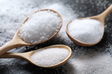 Photo of Organic salt in spoons on black table, closeup