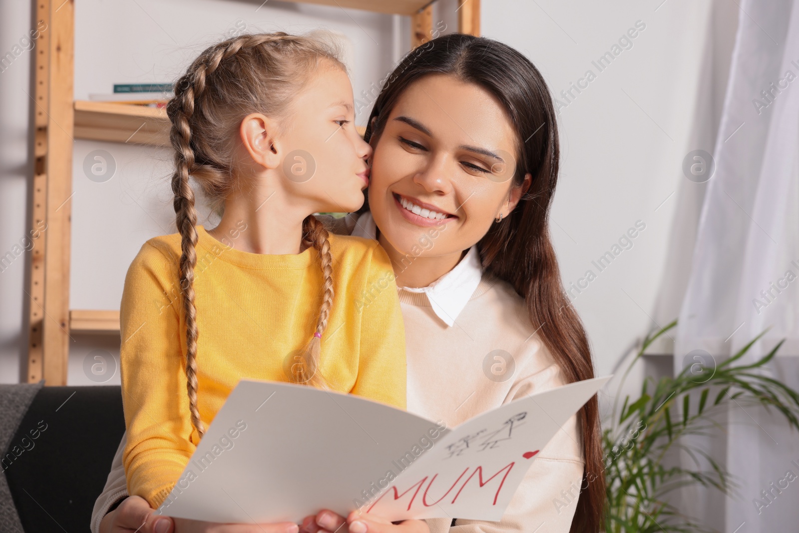 Photo of Happy woman receiving greeting card from her little daughter at home