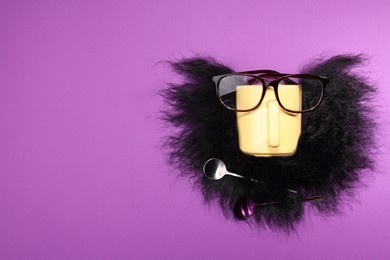 Man's face made of artificial beard, cup and glasses on purple background, top view. Space for text