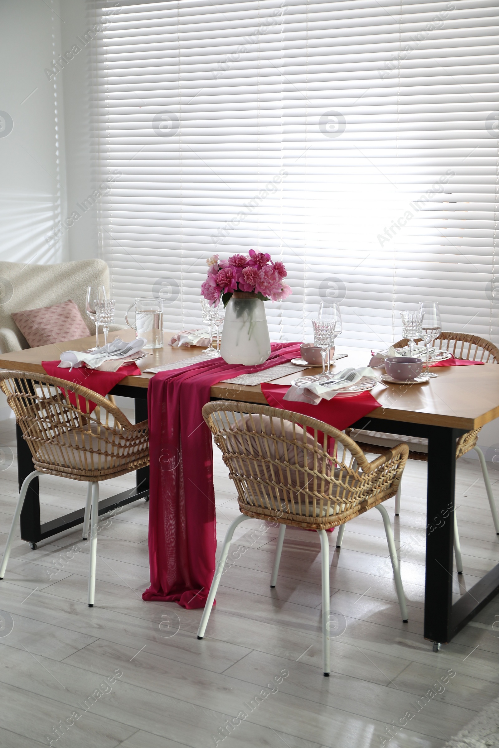 Photo of Pink peonies on table with beautiful setting and rattan chairs in dining room