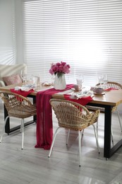 Photo of Pink peonies on table with beautiful setting and rattan chairs in dining room