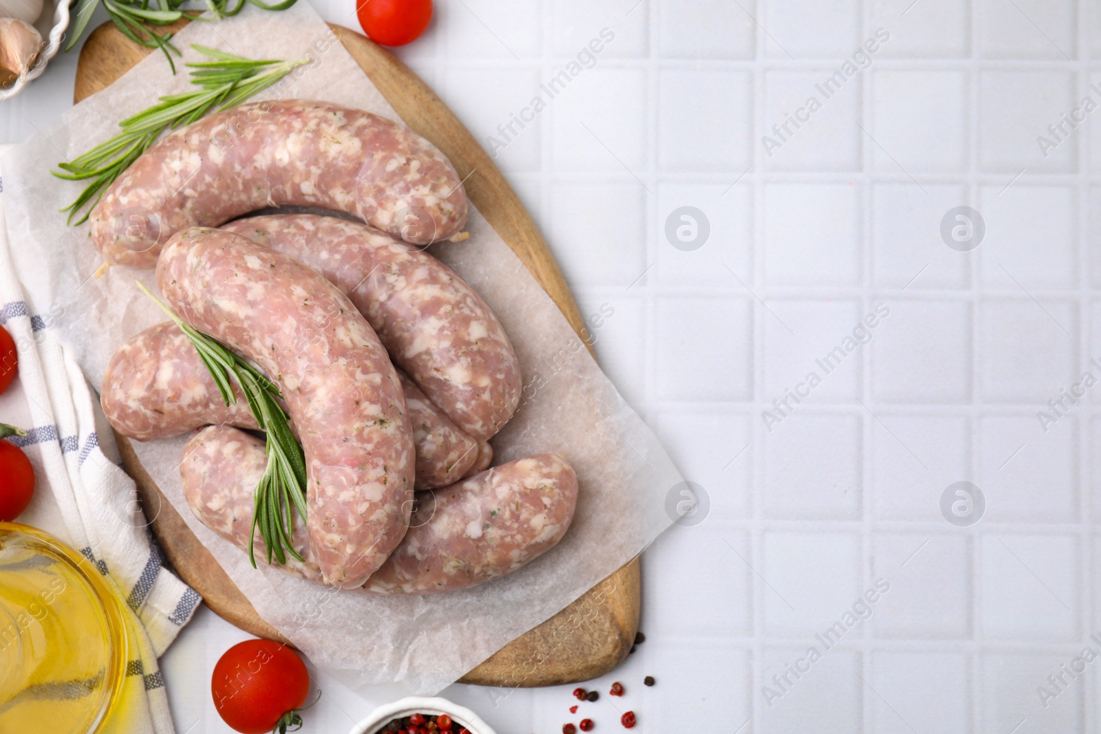 Photo of Raw homemade sausages and different products on white tiled table, flat lay. Space for text