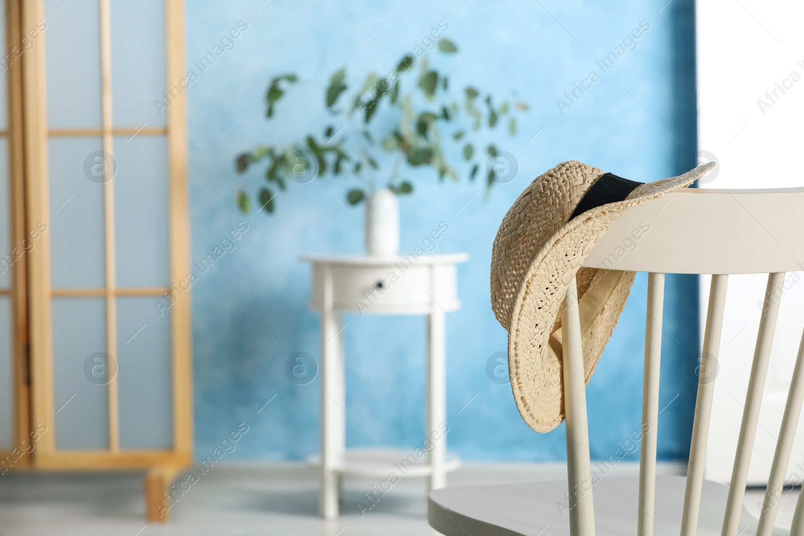 Photo of Stylish straw hat hanging on chair in room, space for text