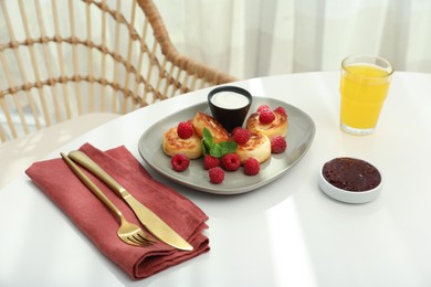 Photo of Delicious cottage cheese pancakes with fresh raspberries, sour cream and mint served on white table indoors