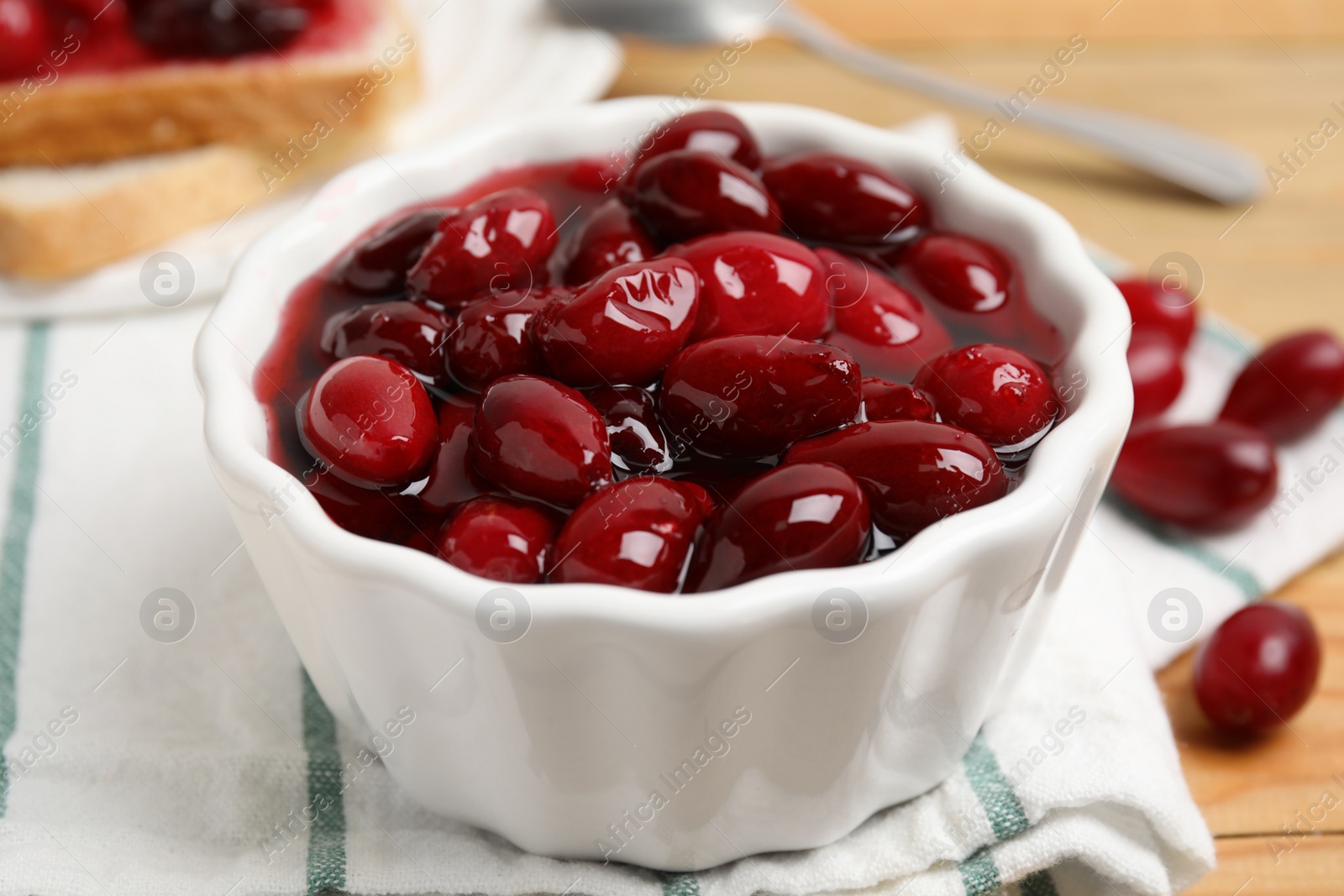 Photo of Delicious dogwood jam with berries in bowl on table, closeup