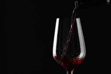 Photo of Pouring red wine into glass against black background, closeup. Space for text