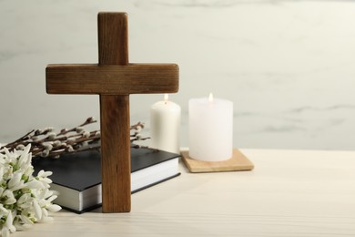 Wooden cross, Bible, church candles, willow branches and snowdrops on white table. Space for text