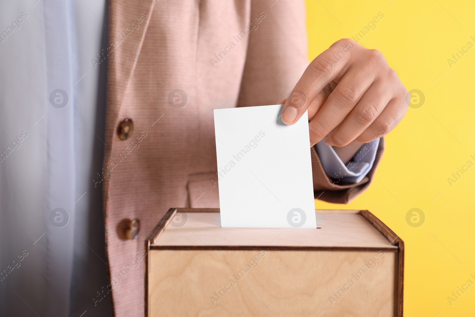 Photo of Woman putting her vote into ballot box on orange background, closeup