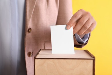 Woman putting her vote into ballot box on orange background, closeup