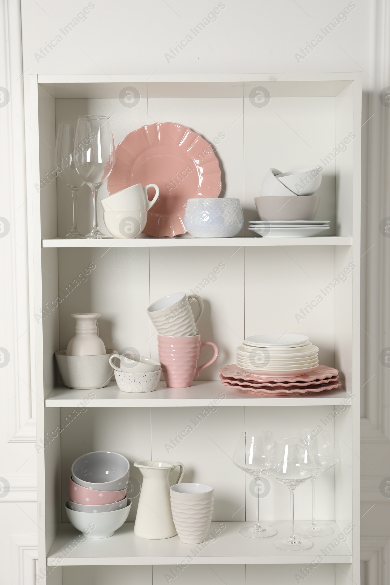 Photo of Different ceramic dishware and glasses on shelves in cabinet indoors