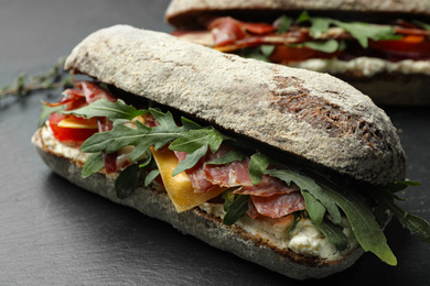 Photo of Delicious sandwich with fresh vegetables and prosciutto on grey table, closeup