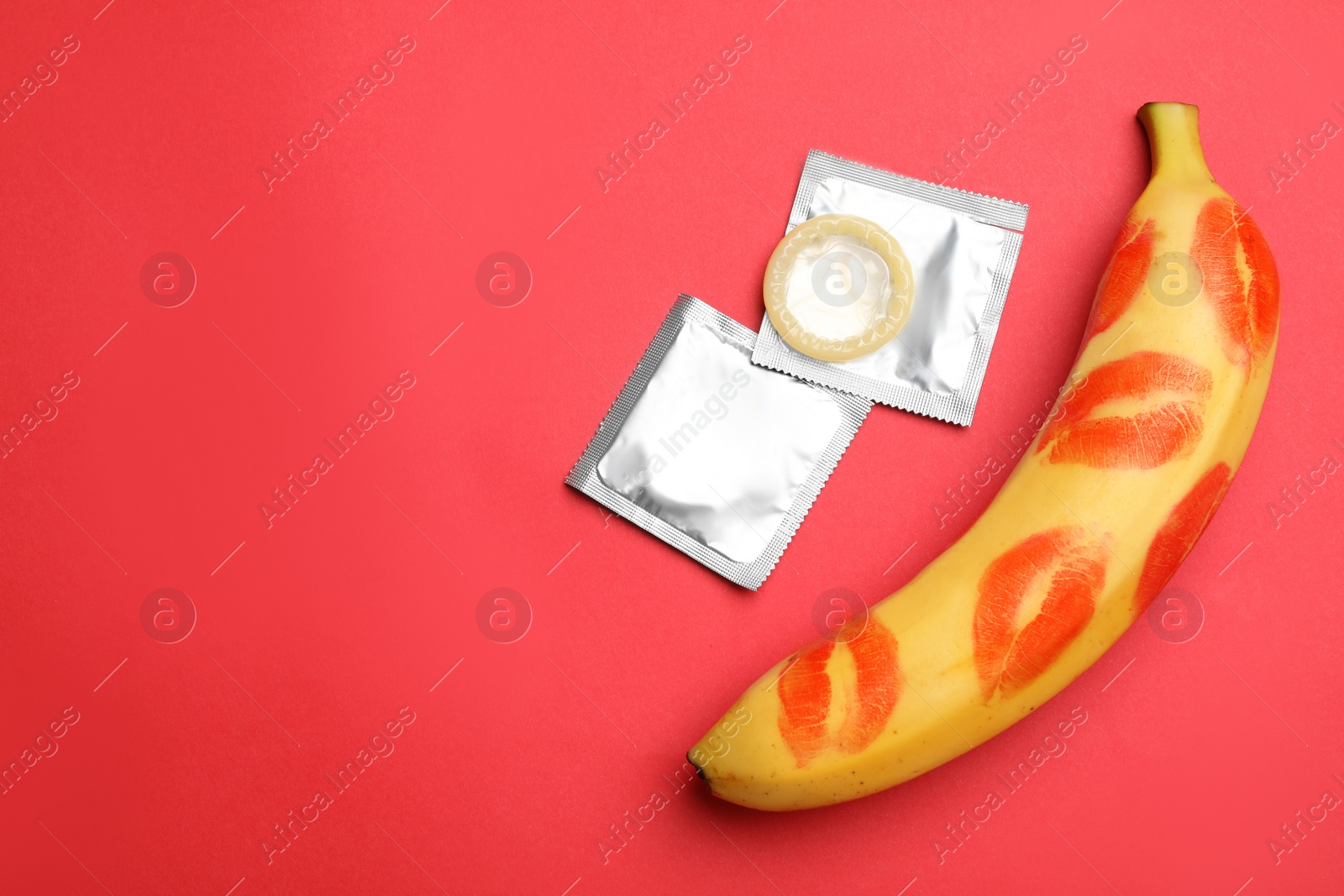 Photo of Condoms, banana with lipstick kiss marks and space for text on red background, flat lay. Safe sex