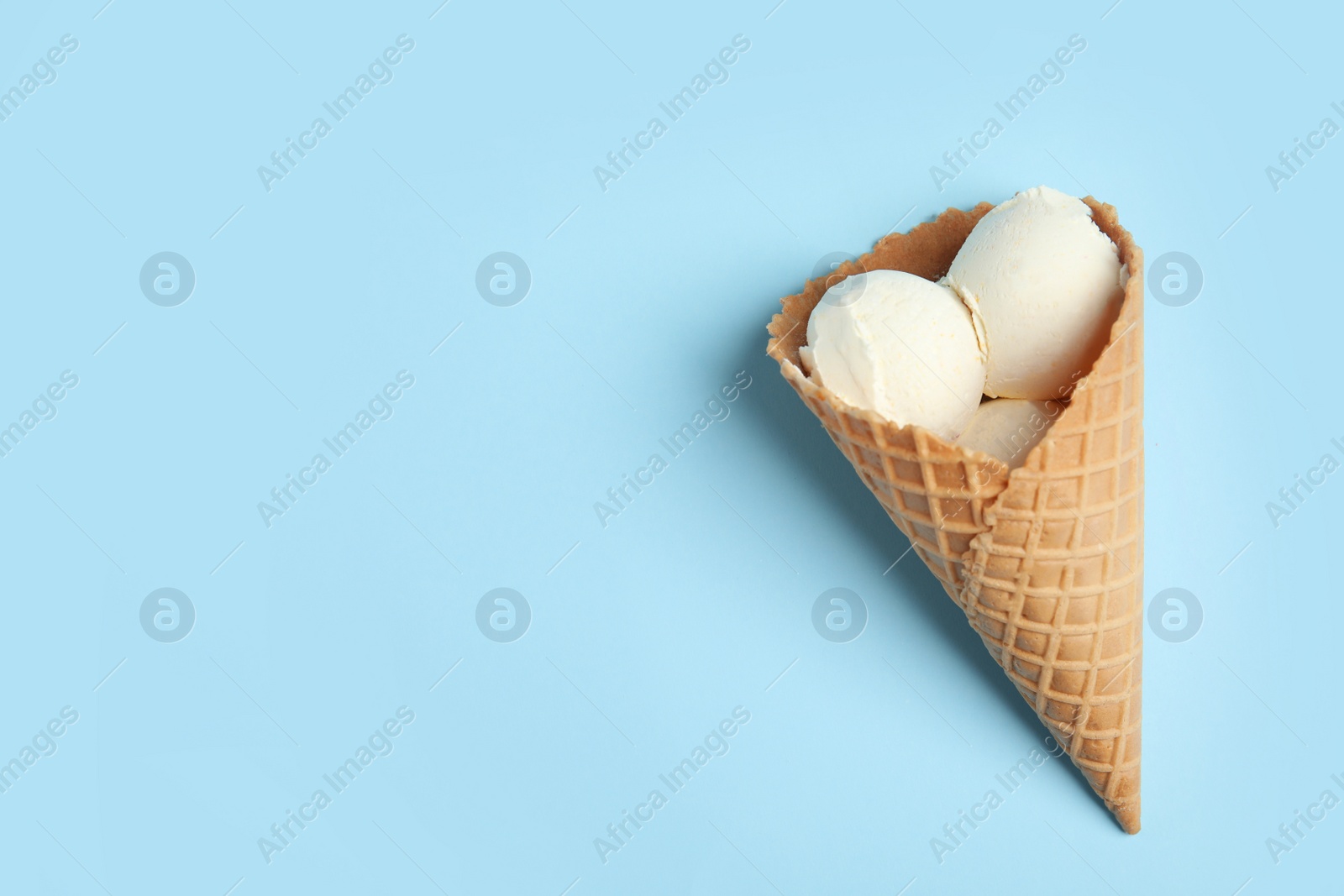 Photo of Delicious vanilla ice cream in wafer cone on blue background, top view. Space for text
