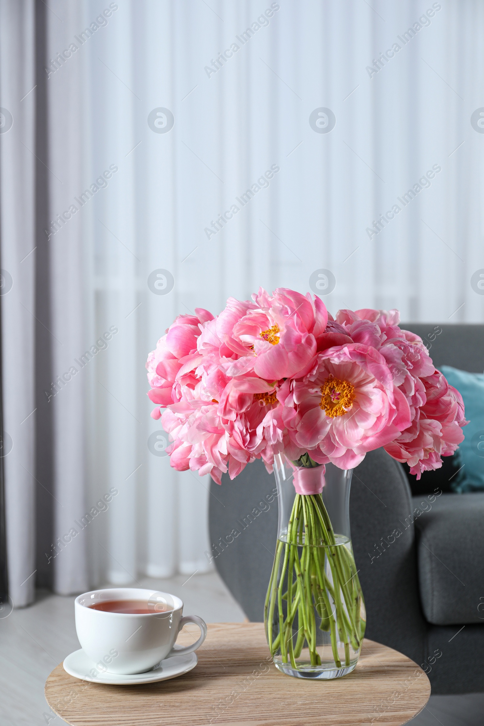 Photo of Beautiful bouquet of pink peonies in vase and cup with drink on wooden table indoors