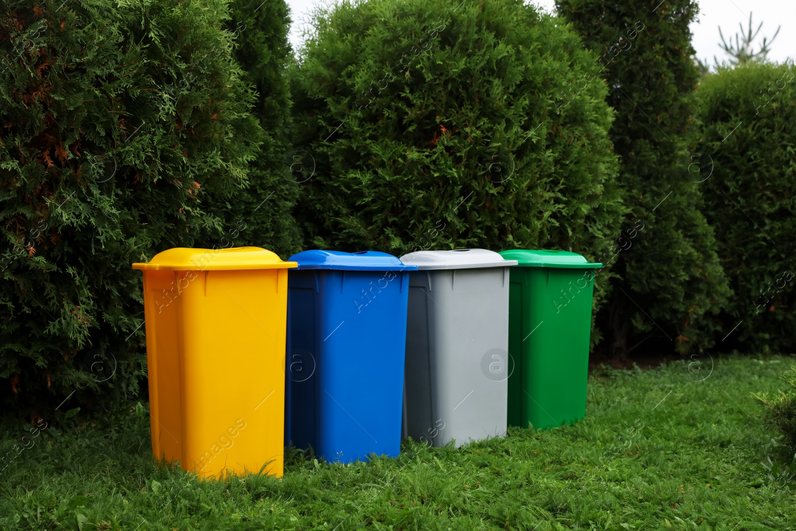 Photo of Many color recycling bins on green grass outdoors, space for text