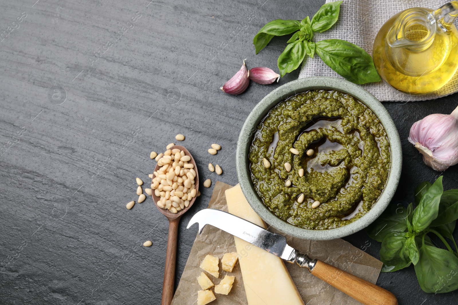 Photo of Tasty pesto sauce, basil, pine nuts, cheese, garlic and oil on black table, flat lay. Space for text