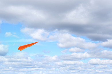 Image of Orange paper plane flying in blue sky with clouds